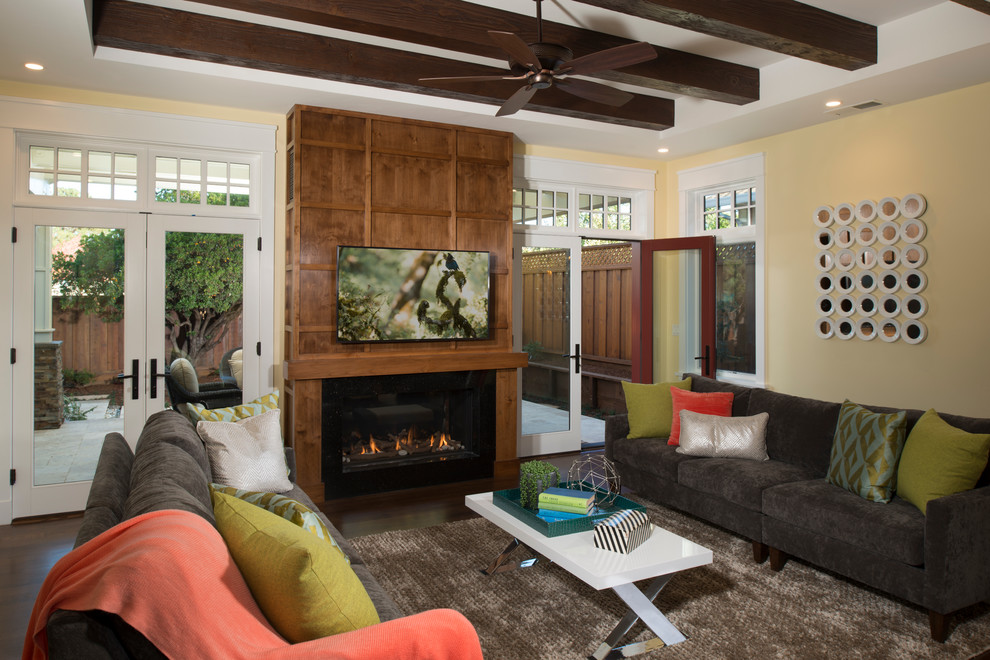 Idée de décoration pour une salle de séjour craftsman de taille moyenne et ouverte avec un mur jaune, un sol en bois brun, une cheminée double-face, un manteau de cheminée en bois, un téléviseur fixé au mur et un sol marron.
