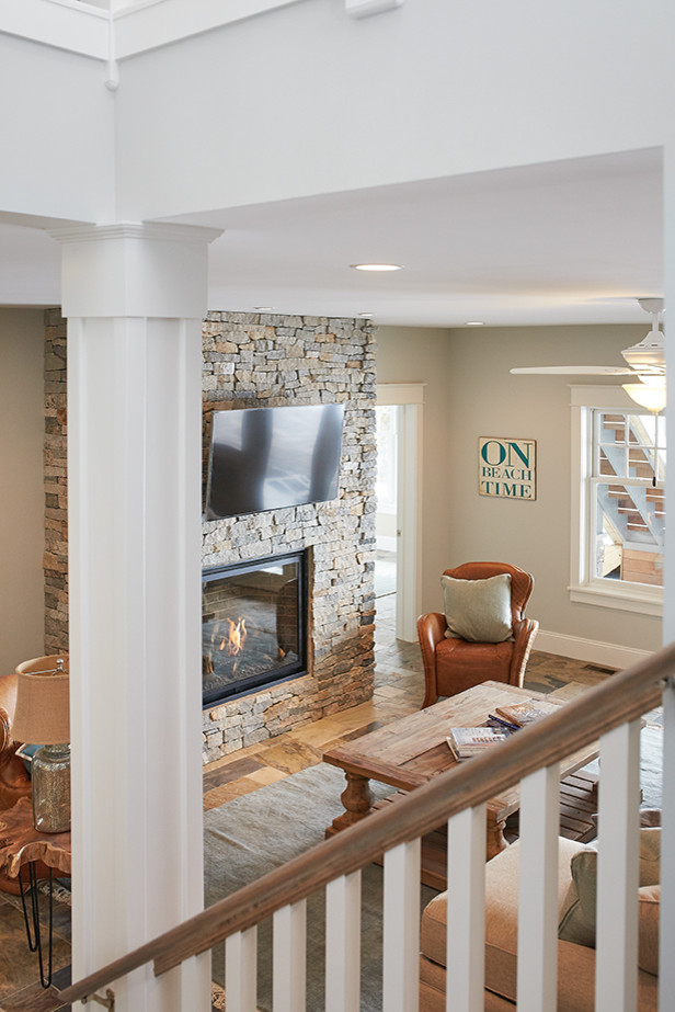 Пример оригинального дизайна: открытая гостиная комната среднего размера в морском стиле с серыми стенами, полом из сланца, стандартным камином, фасадом камина из камня и телевизором на стене