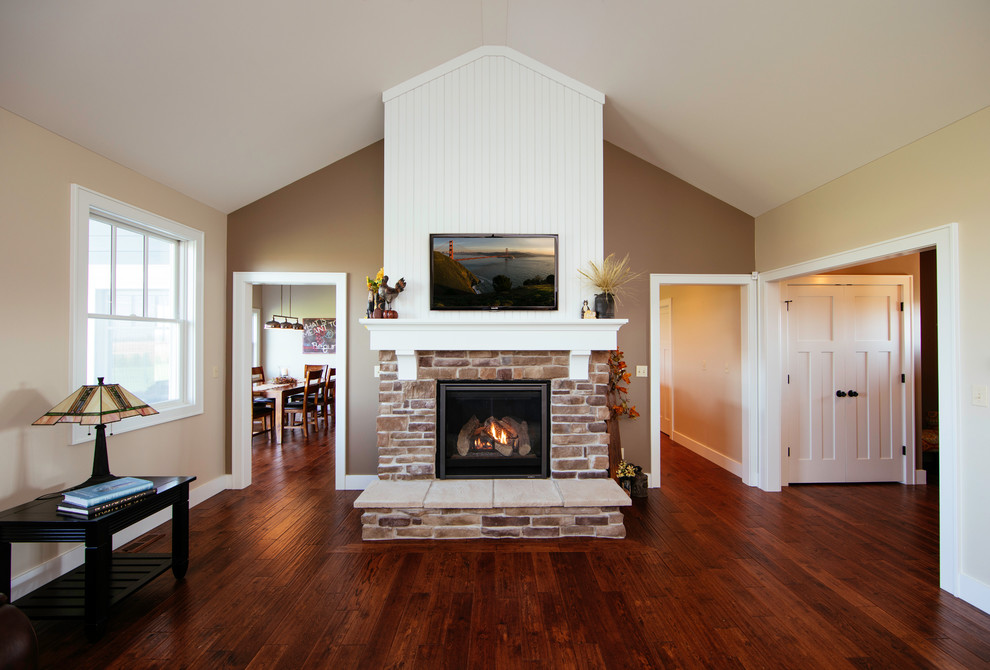 Imagen de sala de estar de estilo de casa de campo con paredes beige, suelo de madera en tonos medios, todas las chimeneas, marco de chimenea de ladrillo y televisor colgado en la pared