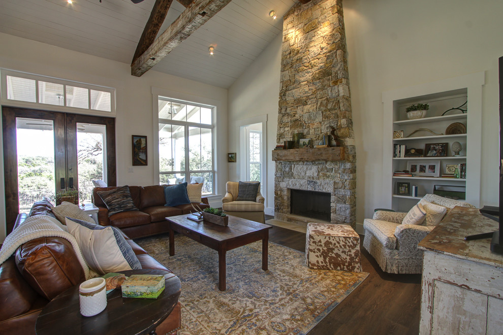 Large rural open plan games room in Austin with white walls, a stone fireplace surround, a freestanding tv, dark hardwood flooring, no fireplace and brown floors.