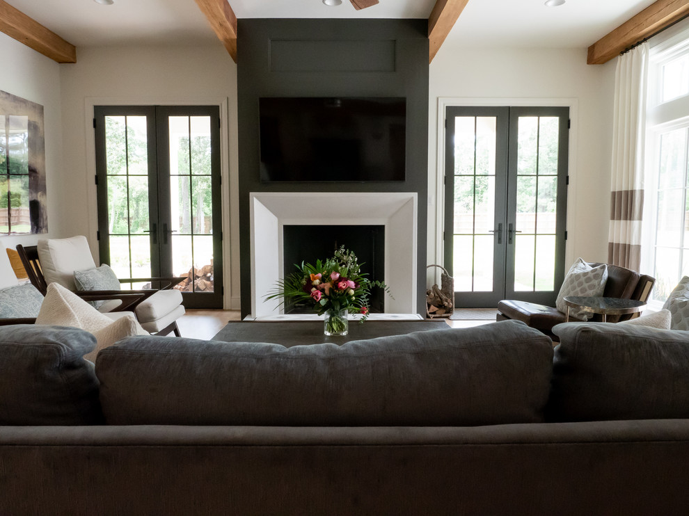 Immagine di un soggiorno country aperto con pareti beige, parquet chiaro, camino classico, TV a parete e cornice del camino in legno