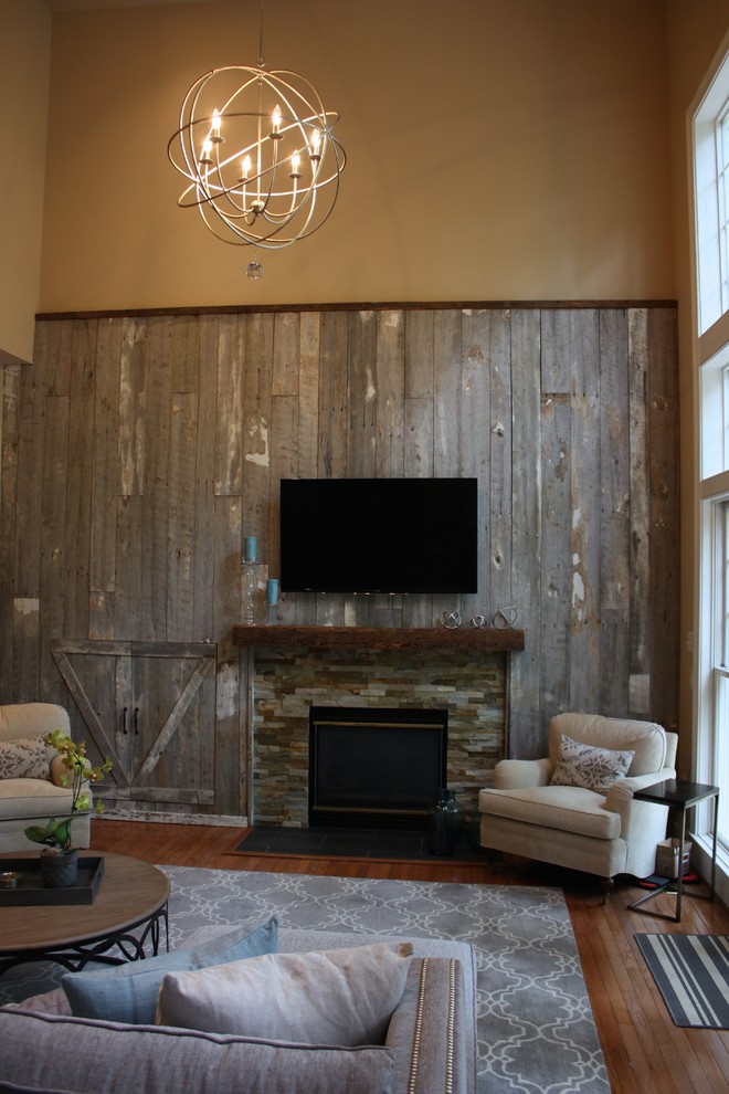 Ejemplo de sala de estar abierta de estilo de casa de campo de tamaño medio con paredes beige, suelo de madera en tonos medios, todas las chimeneas, marco de chimenea de piedra y televisor colgado en la pared