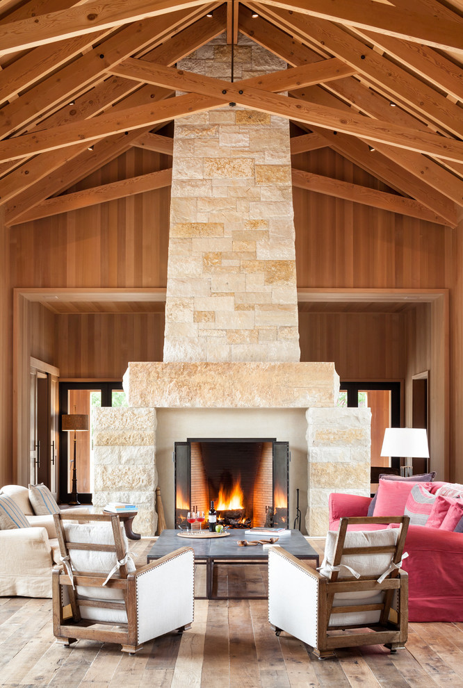 Modelo de sala de estar abierta de estilo de casa de campo extra grande con suelo de madera en tonos medios, marco de chimenea de piedra y todas las chimeneas
