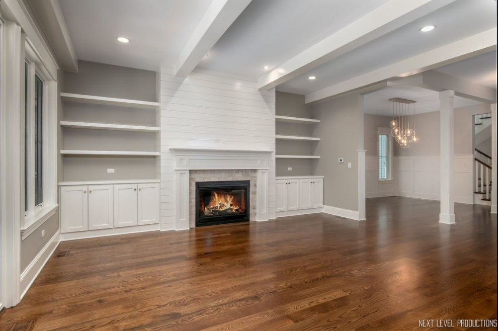 Inspiration for a medium sized country open plan games room in Chicago with a reading nook, grey walls, medium hardwood flooring, a standard fireplace, a timber clad chimney breast, a built-in media unit, brown floors and exposed beams.