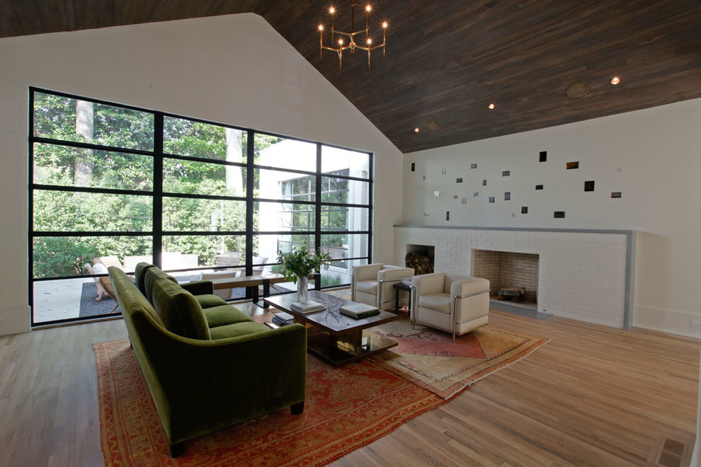На фото: открытая гостиная комната в современном стиле с белыми стенами, светлым паркетным полом, стандартным камином и фасадом камина из кирпича с
