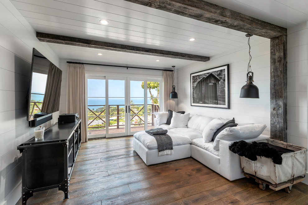 Modelo de sala de estar campestre con paredes blancas, suelo de madera en tonos medios, televisor colgado en la pared y suelo marrón