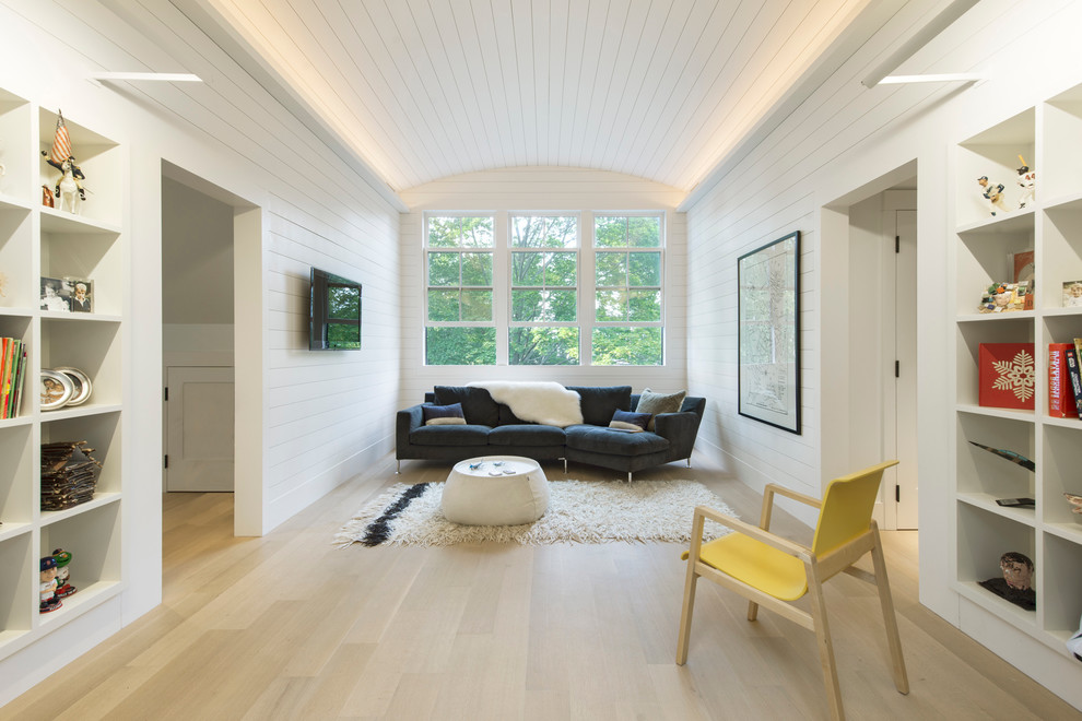 Ejemplo de sala de estar con biblioteca cerrada de estilo de casa de campo con paredes blancas, suelo de madera clara y televisor colgado en la pared