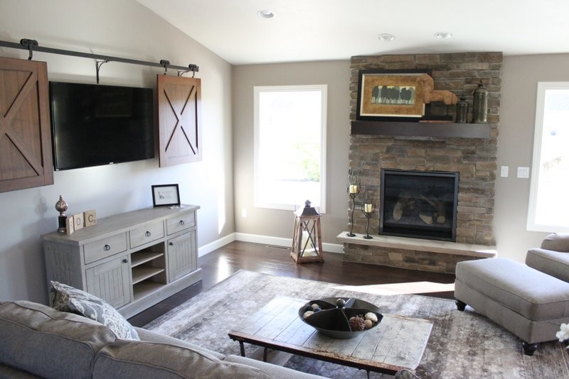 Imagen de sala de estar abierta de estilo de casa de campo grande con paredes grises, suelo de madera oscura, todas las chimeneas, marco de chimenea de piedra y televisor retractable