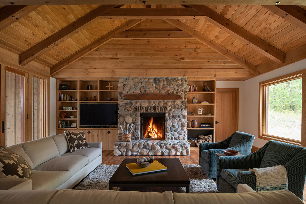 Cette photo montre un salon nature fermé avec un mur blanc, un sol en bois brun, une cheminée standard, un manteau de cheminée en pierre, un téléviseur indépendant et un sol marron.