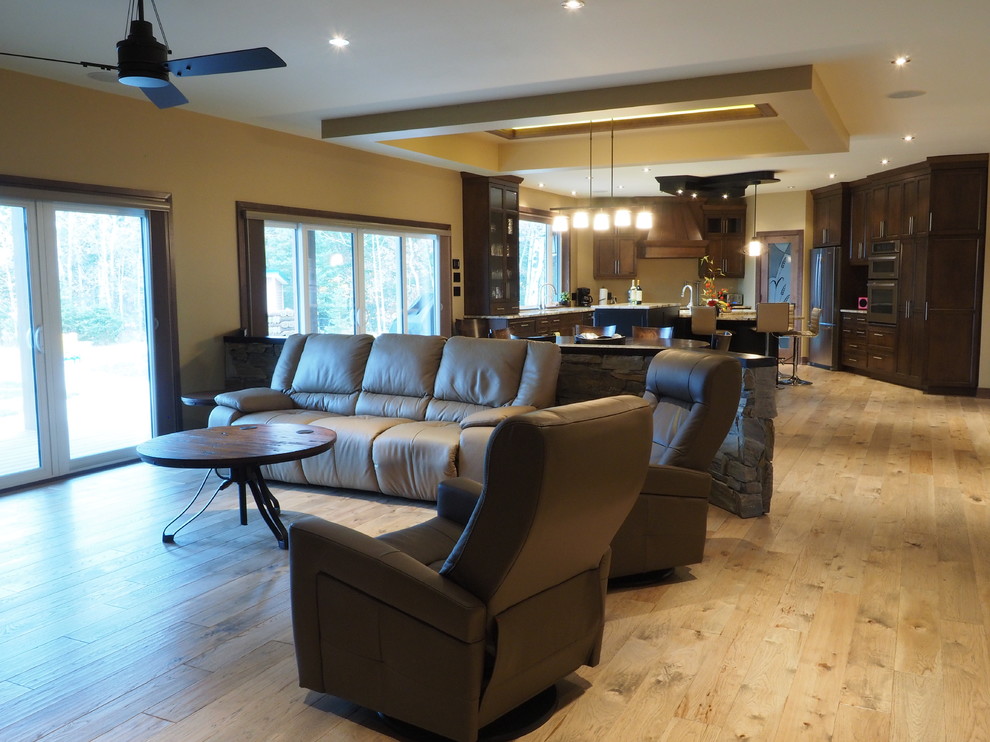 Modelo de sala de estar abierta campestre grande con paredes beige, suelo de madera clara, estufa de leña, marco de chimenea de piedra, pared multimedia y suelo marrón