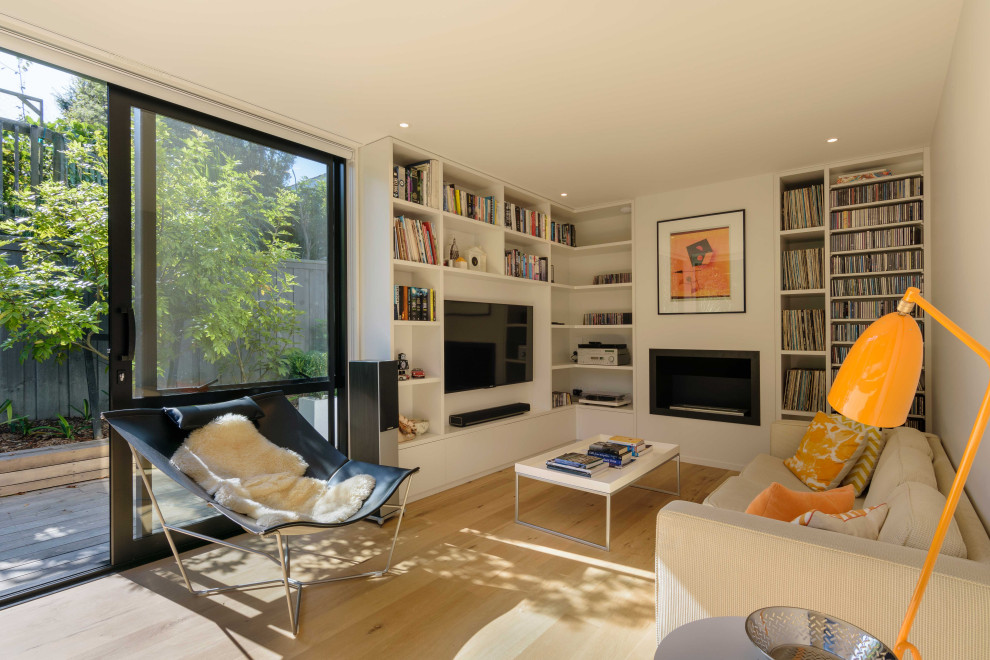 Imagen de sala de estar con biblioteca cerrada actual de tamaño medio con paredes blancas, suelo de madera clara y pared multimedia
