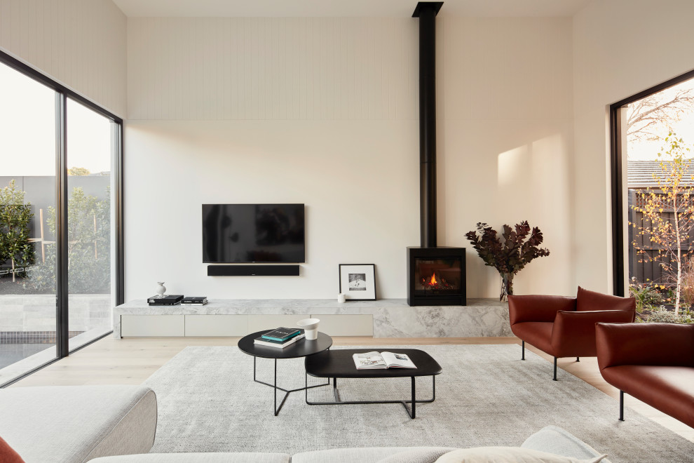 Cette image montre une grande salle de séjour minimaliste ouverte avec un mur blanc, parquet clair, un sol beige, une cheminée standard et un téléviseur fixé au mur.