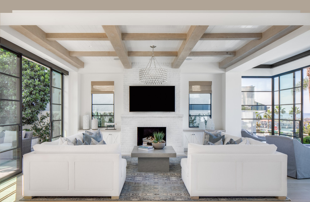 Стильный дизайн: открытая гостиная комната в морском стиле с белыми стенами, светлым паркетным полом, стандартным камином, фасадом камина из кирпича, телевизором на стене и ковром на полу - последний тренд