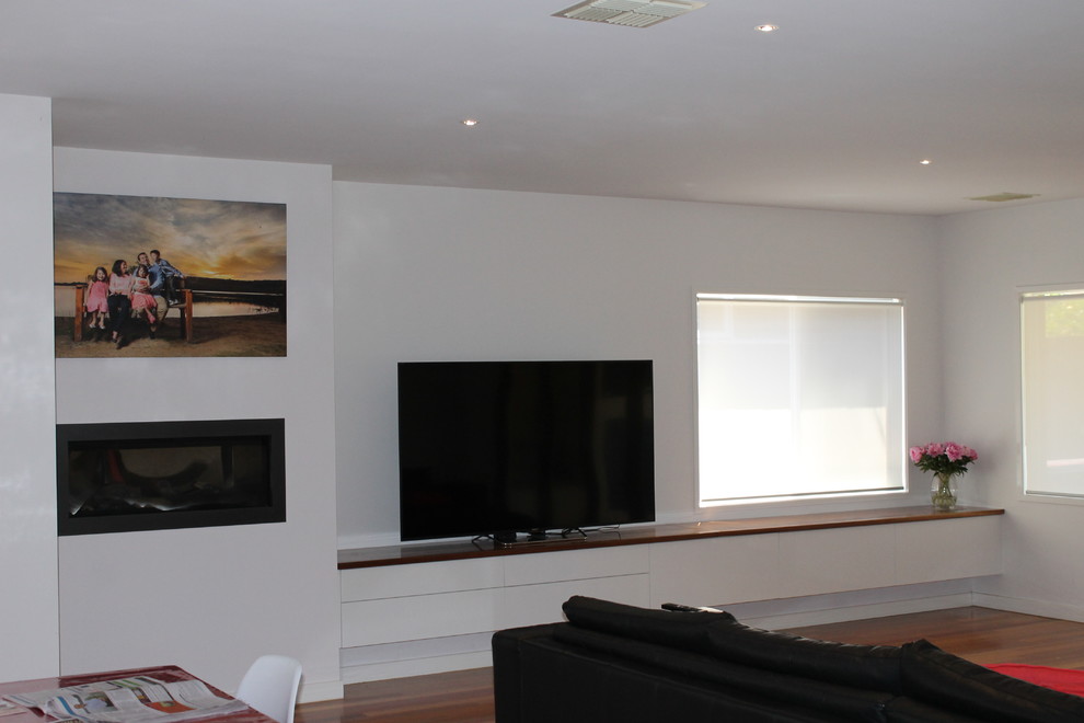 Modelo de sala de estar moderna pequeña con paredes blancas, marco de chimenea de madera, televisor colgado en la pared y todas las chimeneas
