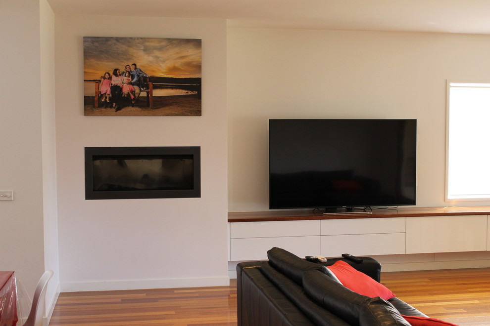Imagen de sala de estar moderna pequeña con paredes blancas, todas las chimeneas, marco de chimenea de madera y televisor colgado en la pared