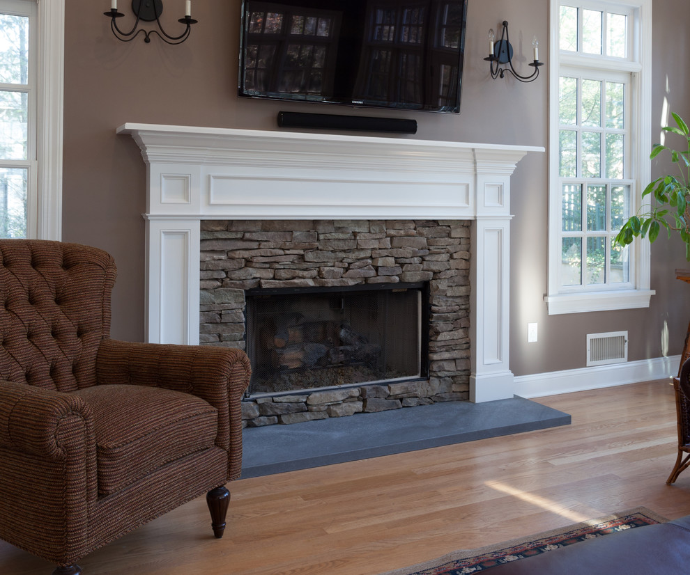 Modelo de sala de estar tradicional de tamaño medio con suelo de madera en tonos medios, todas las chimeneas, marco de chimenea de piedra, televisor colgado en la pared y paredes grises