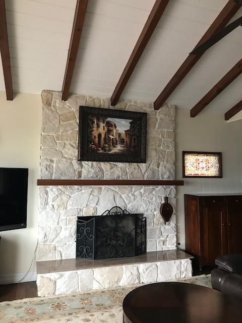 Großes, Offenes Rustikales Wohnzimmer mit beiger Wandfarbe, dunklem Holzboden, Kamin, Kaminumrandung aus Stein, freistehendem TV und braunem Boden in San Diego