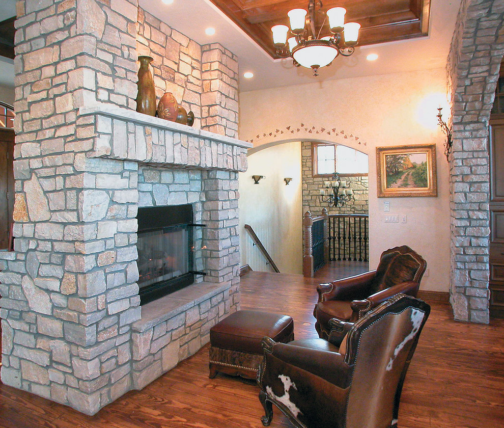 This is an example of a large traditional open plan games room in Other with beige walls, medium hardwood flooring, a two-sided fireplace and a stone fireplace surround.