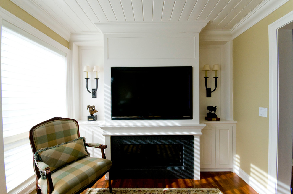 Kleines, Abgetrenntes Klassisches Wohnzimmer mit gelber Wandfarbe, braunem Holzboden, Kamin, Kaminumrandung aus Stein und Multimediawand in Minneapolis