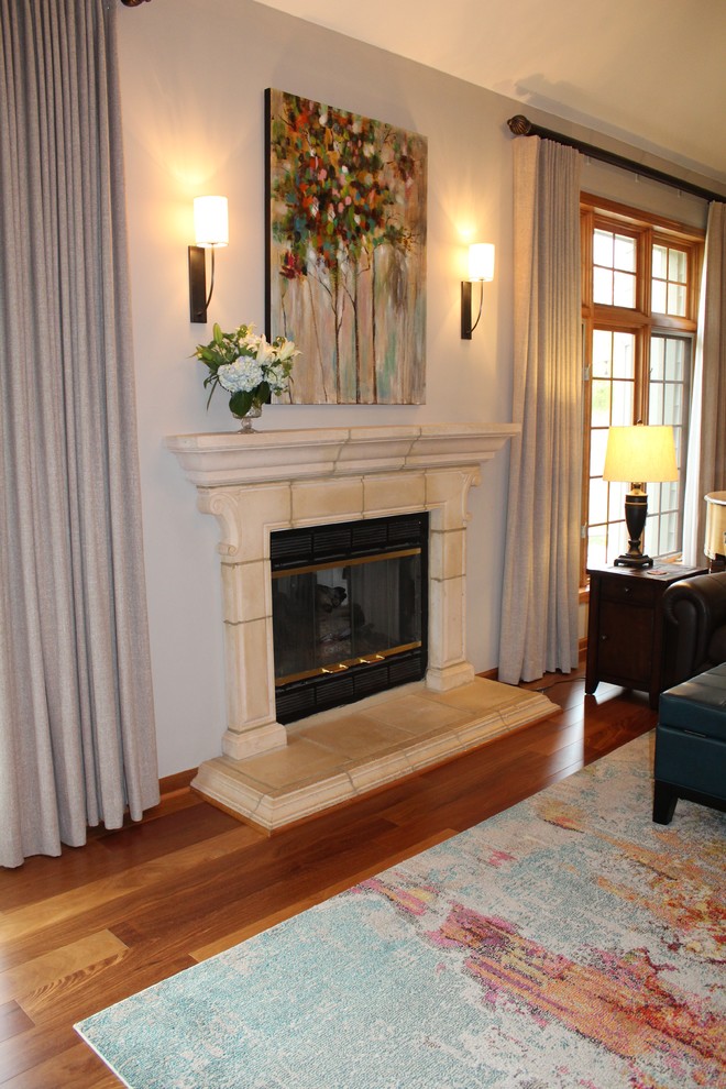 Cette photo montre une grande salle de séjour chic ouverte avec un mur gris, un sol en bois brun, une cheminée standard, un manteau de cheminée en pierre, un téléviseur indépendant et un sol marron.