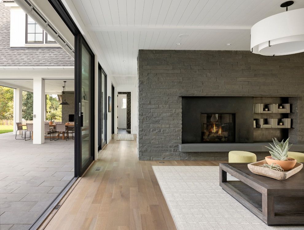 Aménagement d'une salle de séjour contemporaine avec un manteau de cheminée en pierre, un mur gris, parquet clair, une cheminée standard et un sol beige.