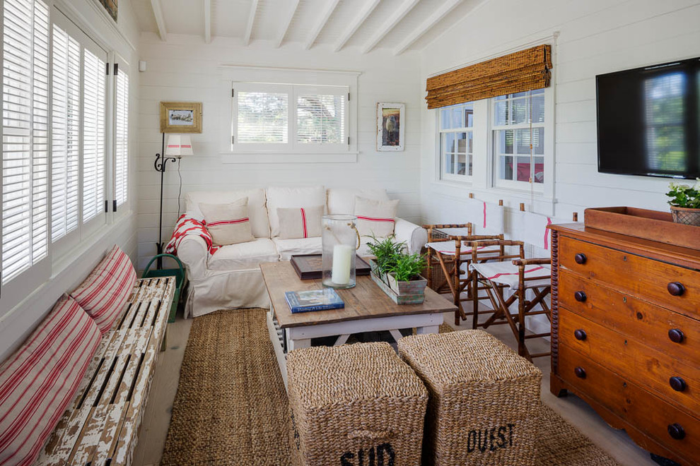 Imagen de sala de estar abierta costera pequeña sin chimenea con paredes blancas, suelo de madera clara y televisor colgado en la pared