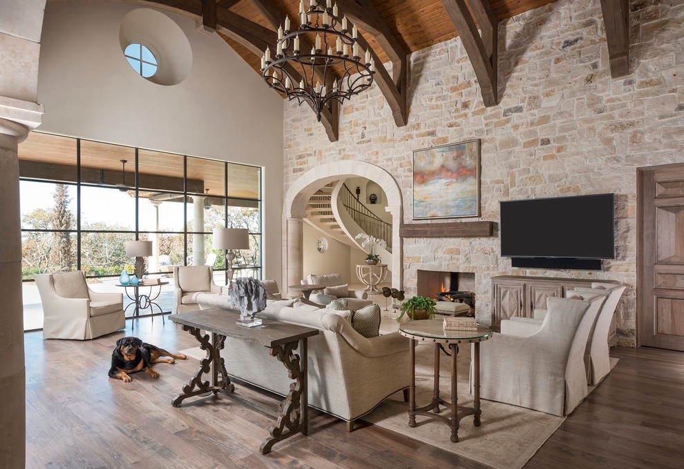 Geräumiges Mediterranes Wohnzimmer mit Kamin, Kaminumrandung aus Stein, TV-Wand und braunem Holzboden in Dallas