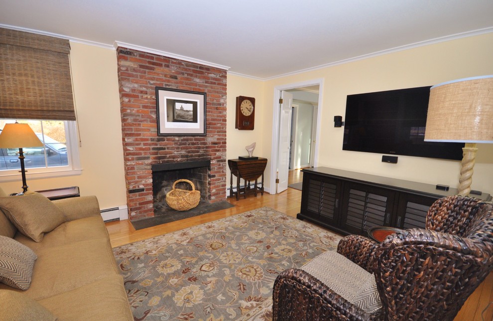 ブリッジポートにある小さなエクレクティックスタイルのおしゃれな独立型ファミリールーム (黄色い壁、無垢フローリング、標準型暖炉、レンガの暖炉まわり、壁掛け型テレビ、茶色い床) の写真