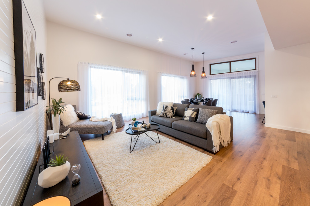 Cette image montre une grande salle de séjour design ouverte avec un mur blanc, sol en stratifié et un sol marron.