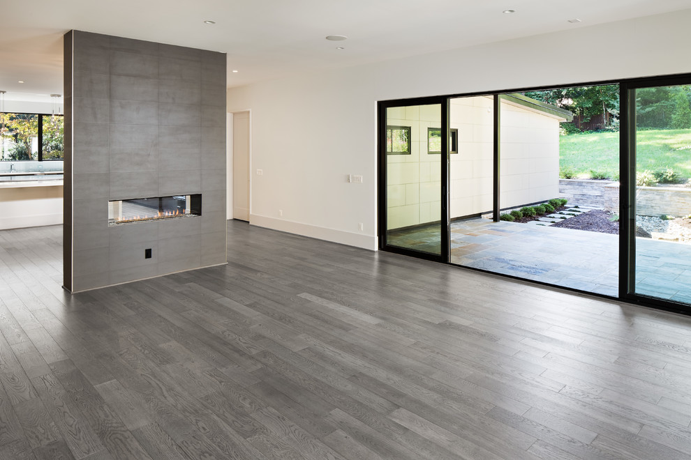 Example of a large minimalist open concept light wood floor and brown floor family room design in DC Metro with white walls, a two-sided fireplace, a tile fireplace and a media wall