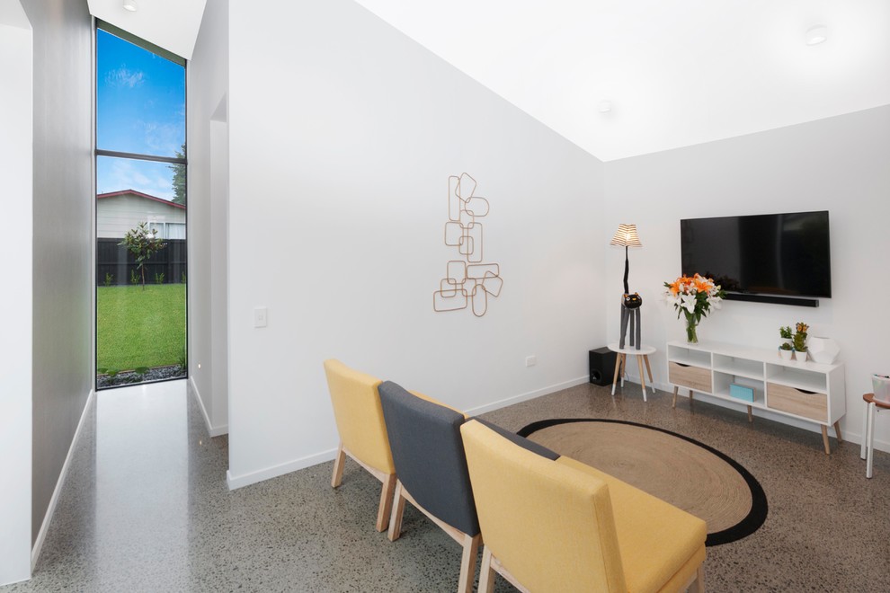 Ejemplo de sala de estar abierta actual de tamaño medio con paredes blancas, suelo de cemento y televisor colgado en la pared