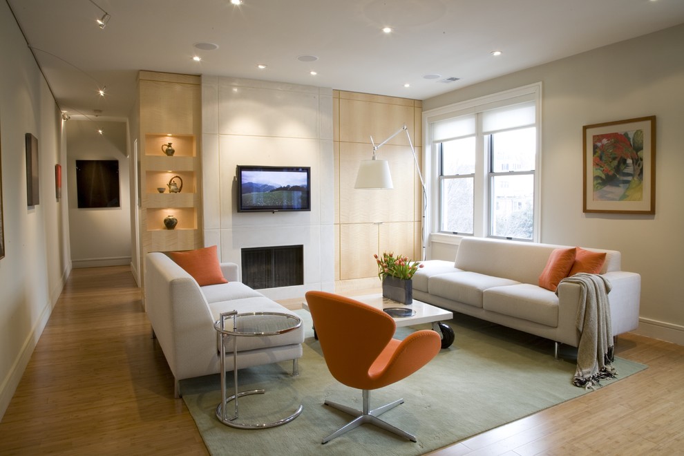 Ejemplo de sala de estar contemporánea con paredes beige, suelo de madera en tonos medios, todas las chimeneas, televisor colgado en la pared y alfombra