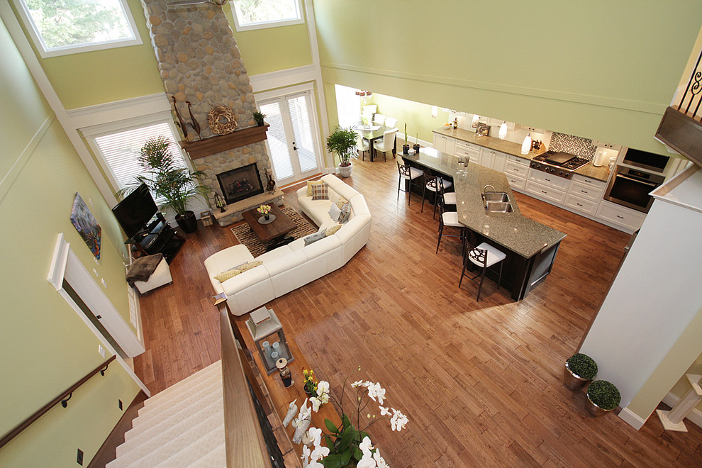 Großes, Offenes Rustikales Wohnzimmer mit grüner Wandfarbe, braunem Holzboden, Kamin, Kaminumrandung aus Stein und freistehendem TV in Vancouver