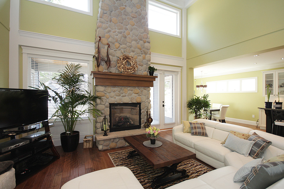 Großes, Offenes Rustikales Wohnzimmer mit braunem Holzboden, Kamin, Kaminumrandung aus Stein, freistehendem TV und grüner Wandfarbe in Vancouver