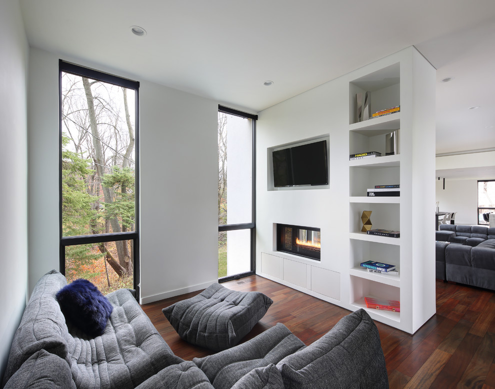Стильный дизайн: гостиная комната в стиле модернизм с белыми стенами, паркетным полом среднего тона, двусторонним камином, телевизором на стене и коричневым полом - последний тренд