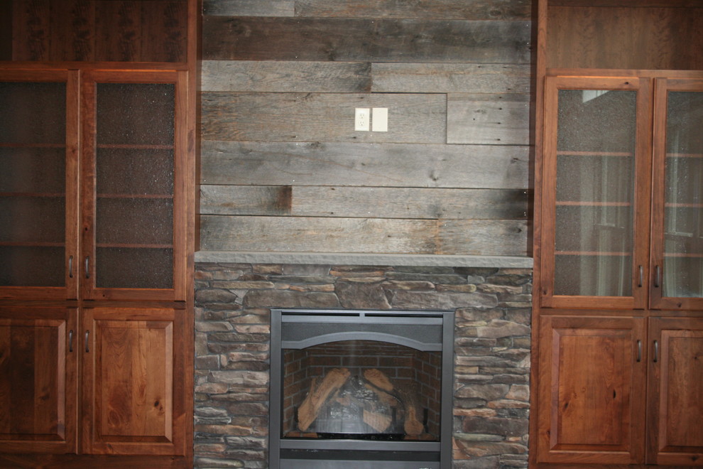 Пример оригинального дизайна: большая открытая гостиная комната в стиле кантри с серыми стенами, темным паркетным полом, стандартным камином, фасадом камина из камня, телевизором на стене и коричневым полом