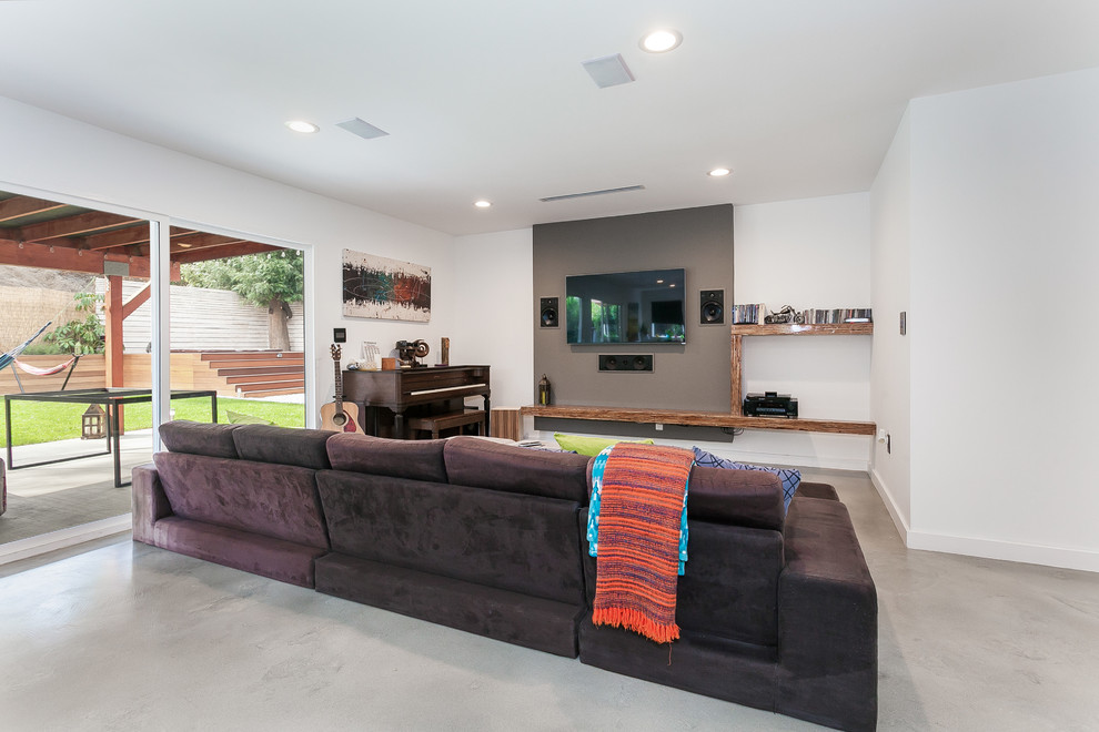 Diseño de sala de estar abierta contemporánea de tamaño medio sin chimenea con paredes blancas, suelo de cemento, televisor colgado en la pared y suelo beige