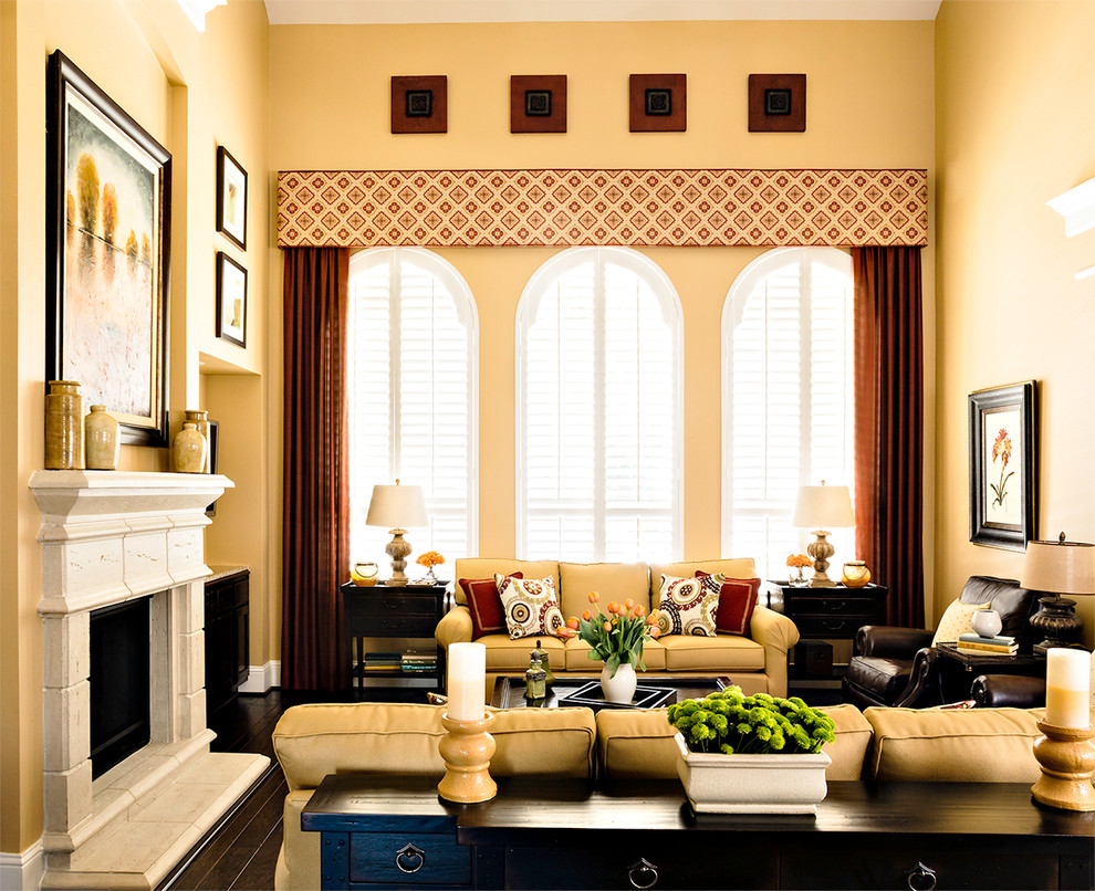 Mittelgroßes, Offenes Klassisches Wohnzimmer mit gelber Wandfarbe, dunklem Holzboden, Kamin, Kaminumrandung aus Beton und Multimediawand in Houston