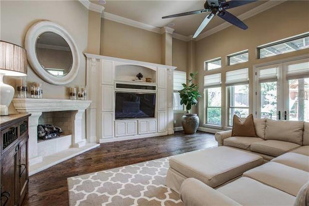Mittelgroßes, Offenes Klassisches Wohnzimmer mit beiger Wandfarbe, dunklem Holzboden, Kamin, Kaminumrandung aus Holz, Multimediawand und braunem Boden in Dallas