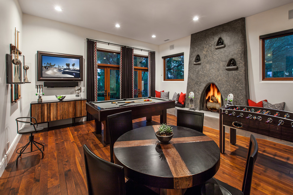 Photo of a large contemporary enclosed games room in Orange County with a game room, white walls, medium hardwood flooring, a standard fireplace, a stone fireplace surround, a wall mounted tv and brown floors.