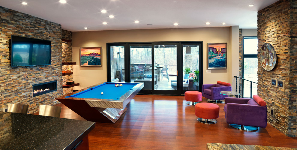 This is an example of a medium sized contemporary mezzanine games room in Cleveland with a game room, brown walls, medium hardwood flooring, a hanging fireplace, a stone fireplace surround, a wall mounted tv and brown floors.