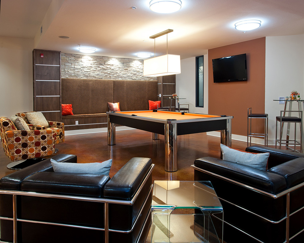 Modelo de sala de juegos en casa abierta contemporánea grande sin chimenea con parades naranjas, suelo de cemento, televisor colgado en la pared y suelo marrón