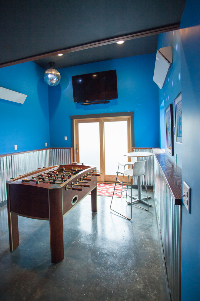 Modelo de sala de juegos en casa cerrada urbana de tamaño medio sin chimenea con paredes azules, suelo de cemento, televisor colgado en la pared y suelo gris