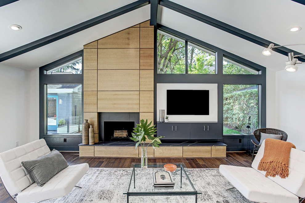 This is an example of a midcentury games room in Houston with white walls, bamboo flooring, a standard fireplace, a wooden fireplace surround, a wall mounted tv and brown floors.