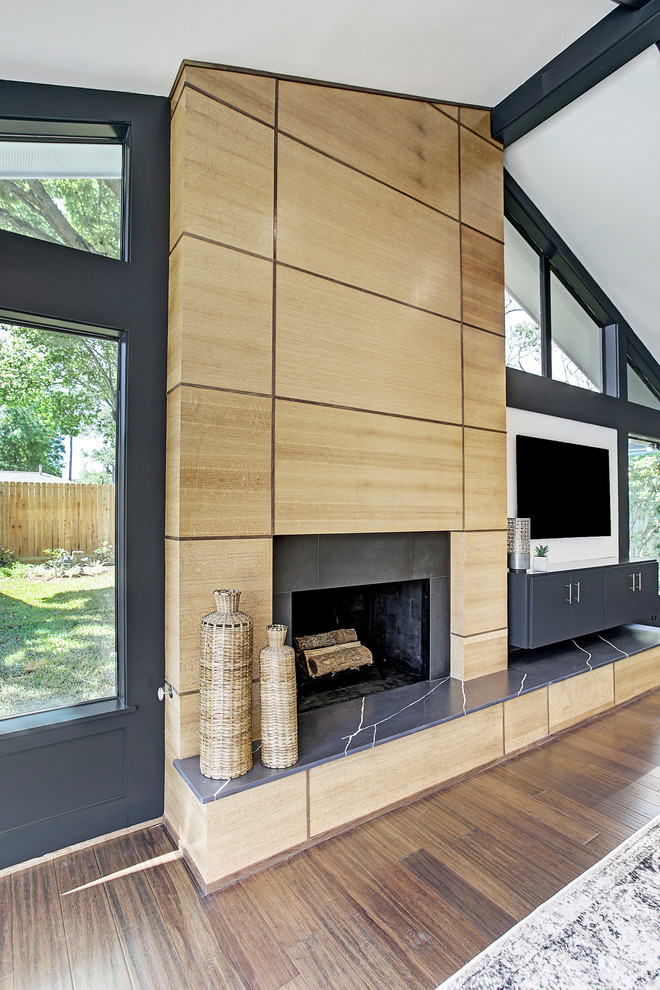 На фото: гостиная комната в стиле ретро с белыми стенами, полом из бамбука, стандартным камином, фасадом камина из дерева, телевизором на стене и коричневым полом