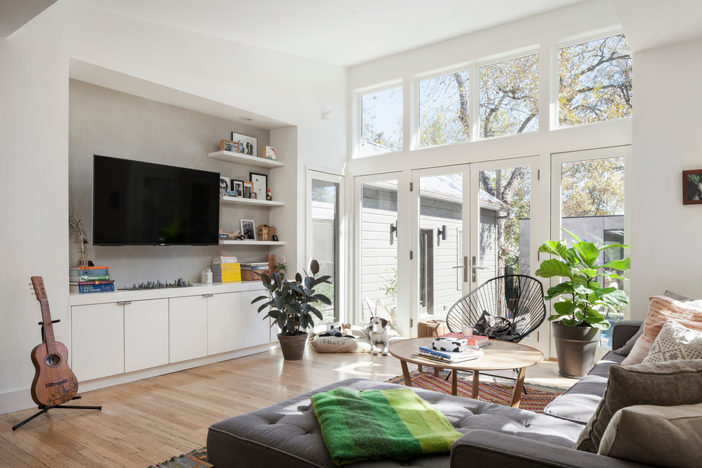 Modelo de sala de estar abierta nórdica de tamaño medio sin chimenea con paredes blancas, suelo de madera clara y televisor colgado en la pared