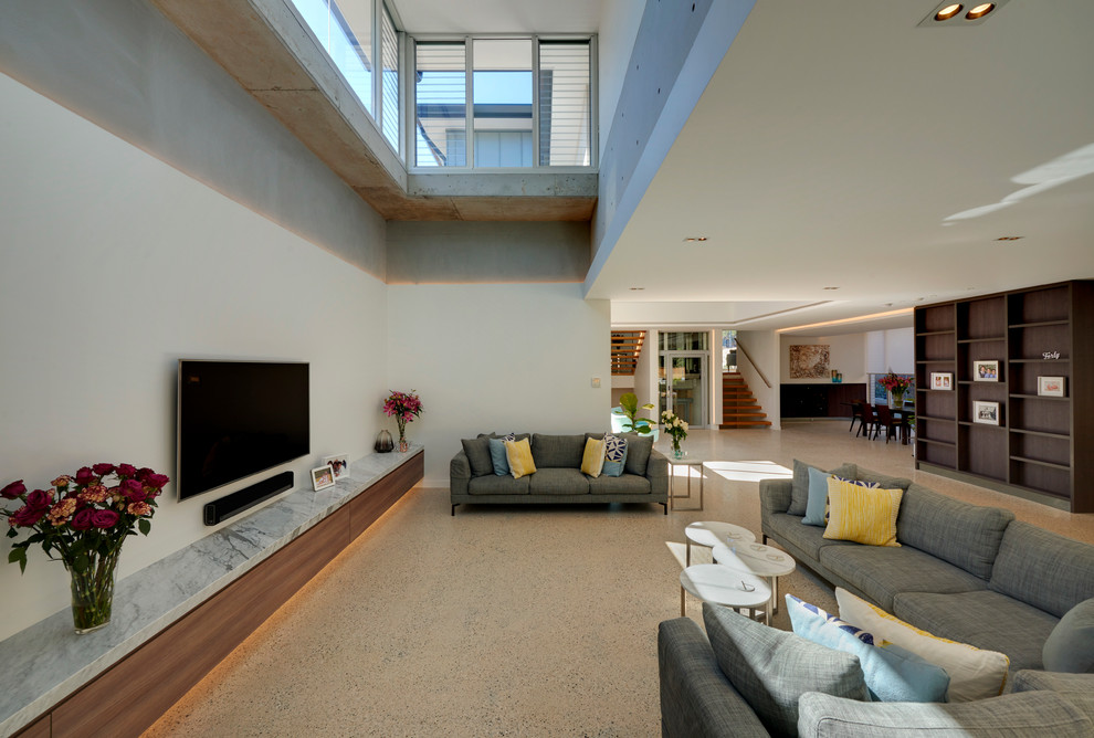 Imagen de sala de estar abierta actual grande sin chimenea con paredes blancas, suelo de cemento y televisor colgado en la pared