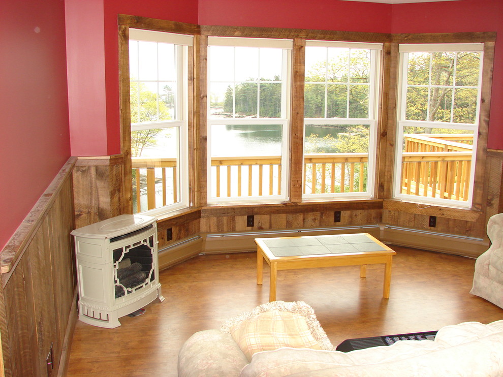 This is an example of a medium sized traditional open plan games room in Portland Maine with red walls, medium hardwood flooring, a wood burning stove and a metal fireplace surround.