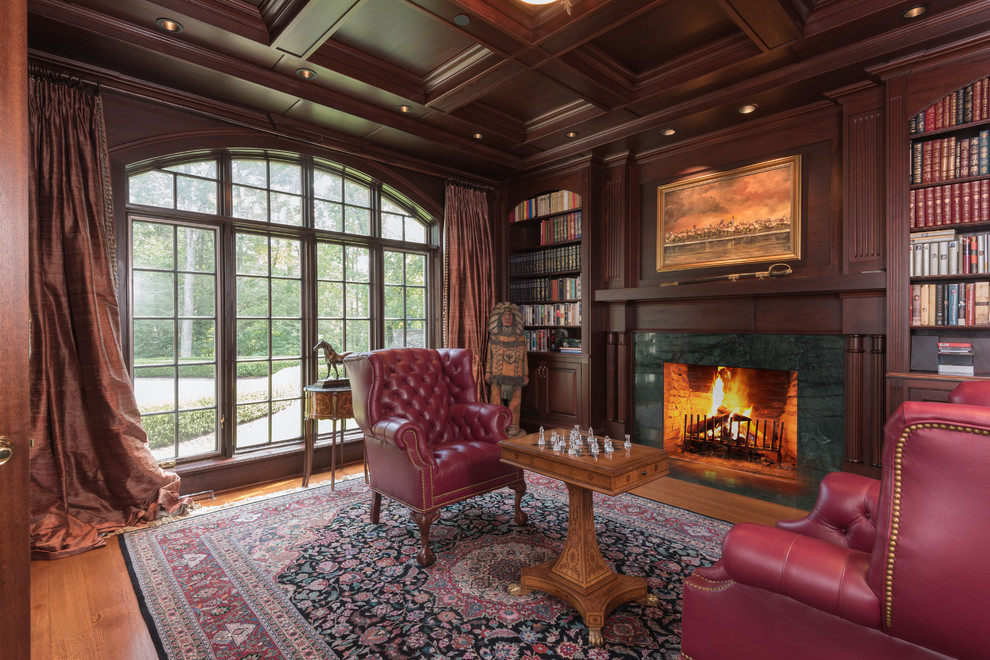 Diseño de sala de estar con biblioteca clásica con suelo de madera en tonos medios, todas las chimeneas, marco de chimenea de piedra y suelo rojo