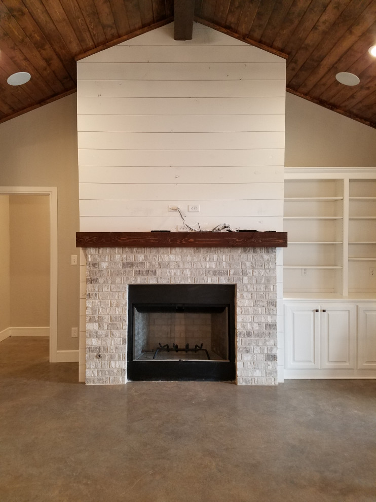 Cette photo montre une salle de séjour nature avec un mur gris, sol en béton ciré, une cheminée standard, un manteau de cheminée en brique, un sol gris, un plafond voûté et du lambris de bois.